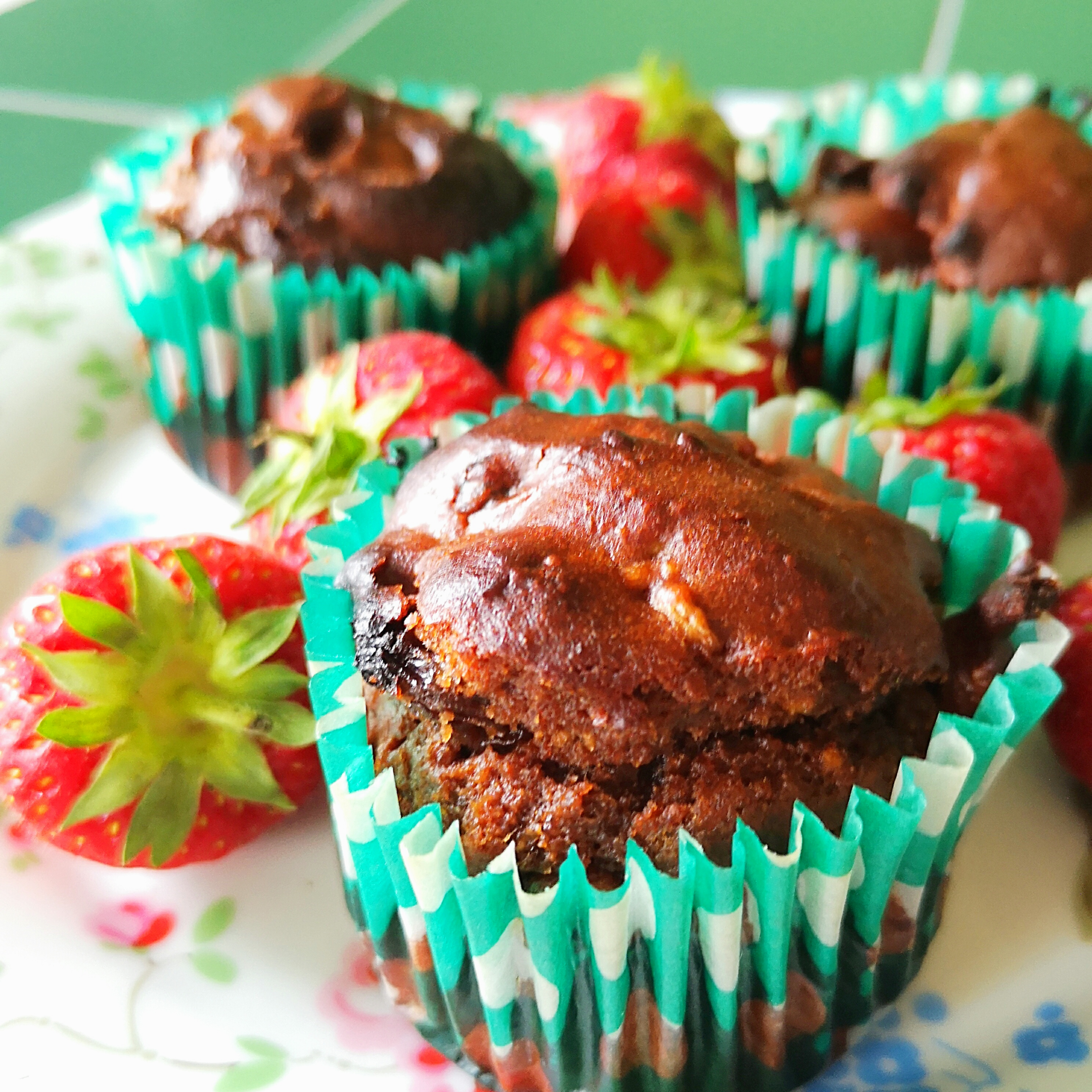 Rich avocado cacao muffins in teal cases with fresh strawberries on a floral plate.