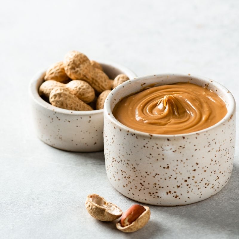 Two small bowls: one with whole peanuts in shells, the other with creamy peanut butter.