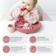 A baby wearing a light pink floral Coverall bib sits in a white high chair with a pink baby weaning plate and matching cup. The image includes feature callouts and icons describing the plate's raised support wall, easy visibility, scoop assist wave, and 360-degree scooping design.