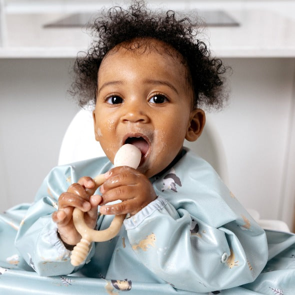 Baby in a blue patterned bib holding a beige Dippit™ multi-stage baby spoon and dipper. - Product image