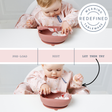 A baby in a pink patterned bib sits in a high chair using a dusty rose silicone suction bowl and spoon. The image is a collage showing three stages: pre-load, rest, and let them try, with a circular badge reading 'Weaning Redefined Tableware'.