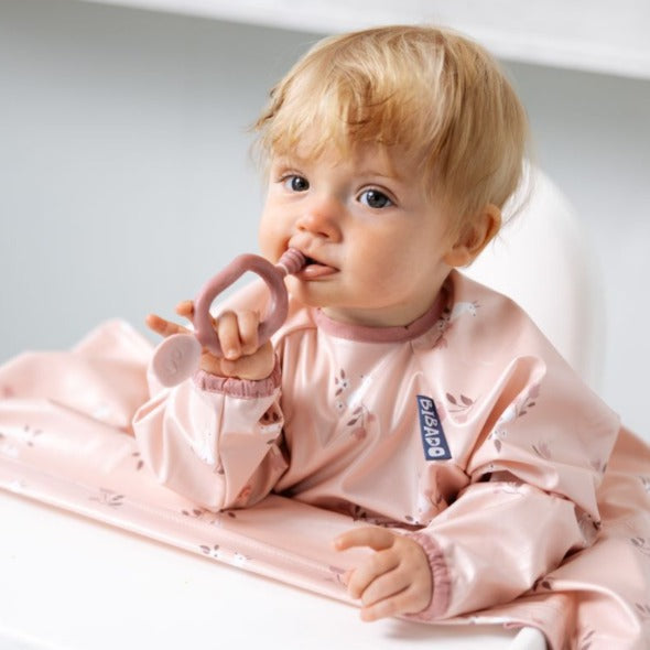 Blonde baby in a pink bib holding a rose-colored Dippit™ multi-stage baby spoon and dipper. - Product image
