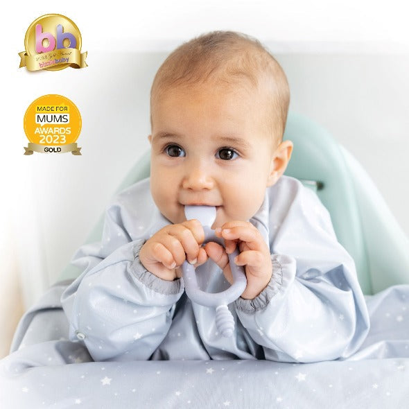 Happy baby in a grey star-patterned bib, holding and chewing a light grey silicone Dippit™ dual-ended spoon. - Product image