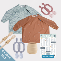 Two long-sleeve weaning bibs (dinosaur print, terracotta rainbow) with various weaning accessories and a food chart.