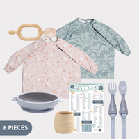 Pink and blue long-sleeve bibs, silicone suction bowl, training cup, cutlery, and weaning chart.
