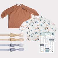 Two long-sleeve weaning bibs: one terracotta with rainbows, one white with construction vehicles. Plus two sets of beige and blue Handi Cutlery, and a First Foods Tick Chart.