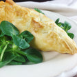 Golden-brown puff pastry turnover with a flaky crust, served on a white plate with fresh green lamb's lettuce.