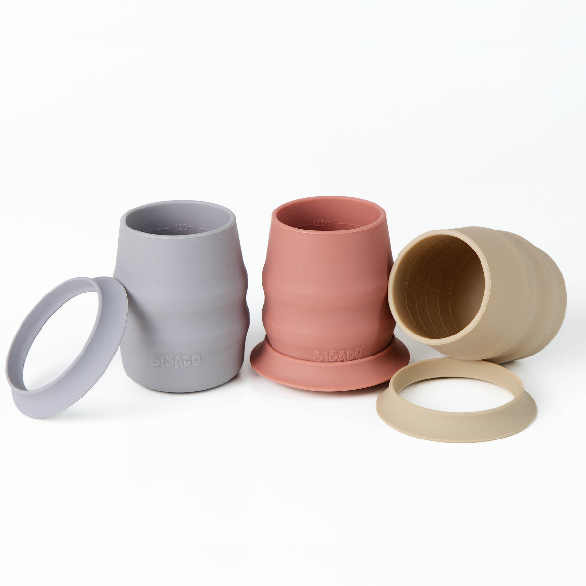 Three silicone open cups in blue, pink, and beige, shown with their matching silicone skirts on a clean white background. - Product image