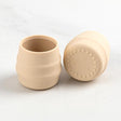 Two small, beige silicone Sippit™ open training cups with ribbed sides and a textured base.
