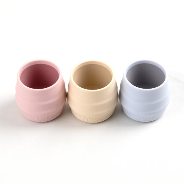 Three small, ribbed silicone Sippit™ open training cups in pink, cream, and light blue. - Product image
