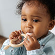 Baby holds a beige silicone Dippit™ dual-ended spoon and textured dipper, wearing a light blue bib.